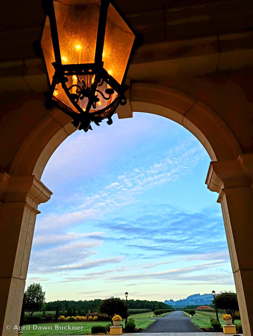 Looking up from under a stone arch with a hanging iron lantern, out to a long path and distant hills