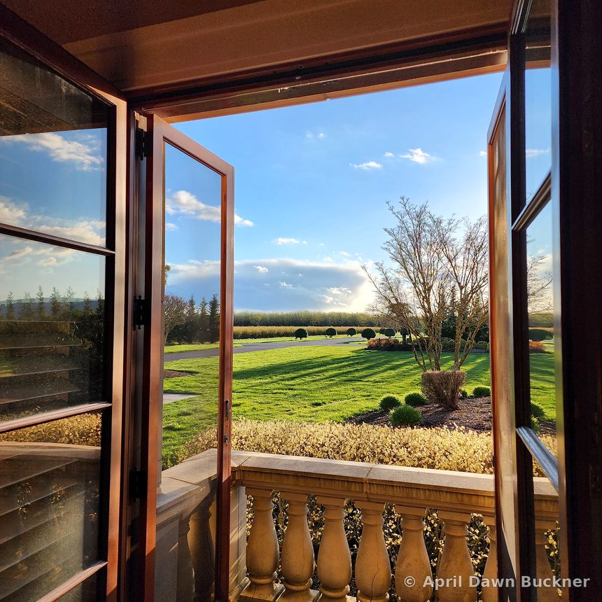 Through open wooden doors onto a balcony with a stone railing, over the striped lawn