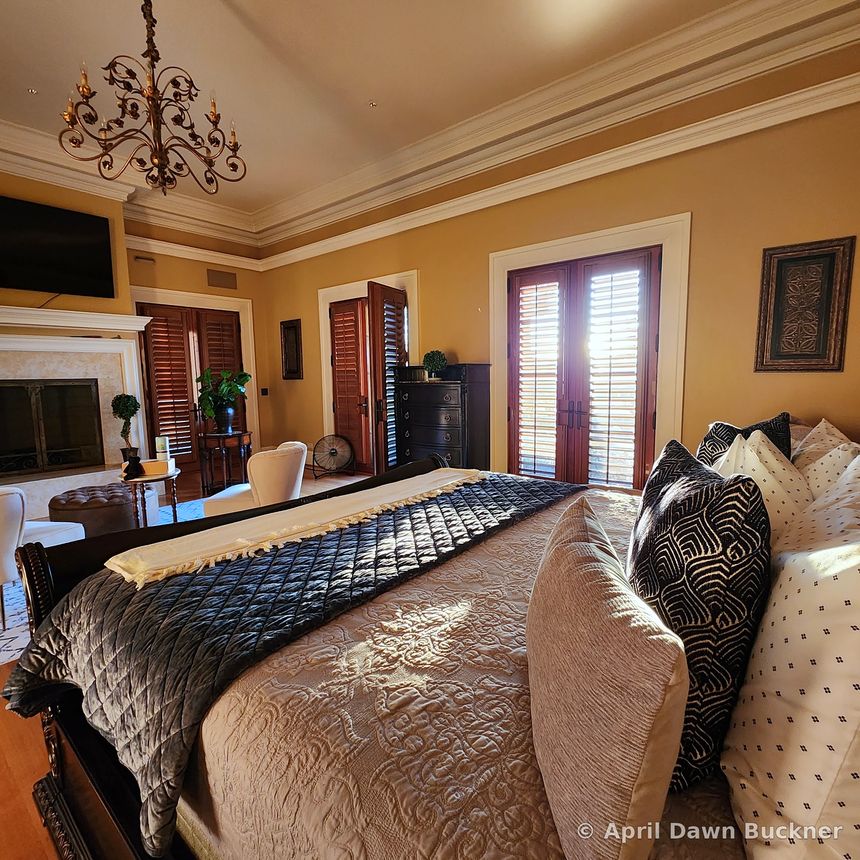 A bedroom with a large bed, a stone fireplace on the left, and French doors to a balcony