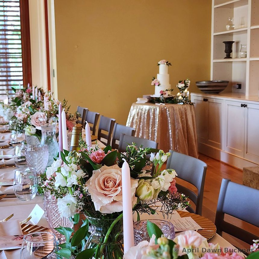 A flower arrangement on a table, with a tiered cake on a draped table behind