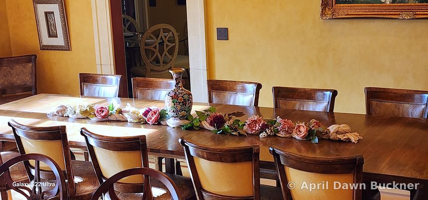 A long wooden table with a centerpiece of pink and white roses and high-backed chairs