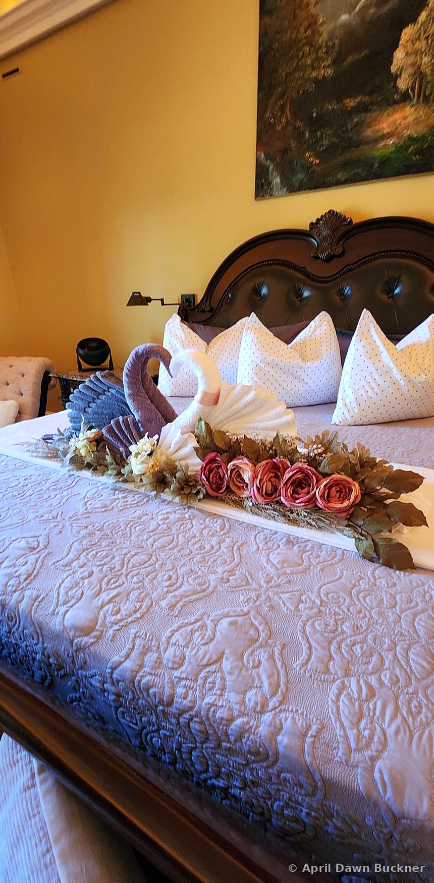 A bed with two towel swans touching heads to form a heart, with a row of pink roses