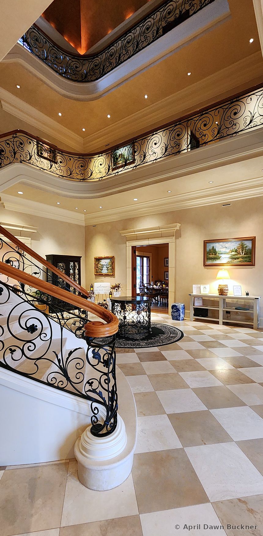 The foyer with a checkered tile floor, a staircase with a wrought-iron rail, and the gallery level above