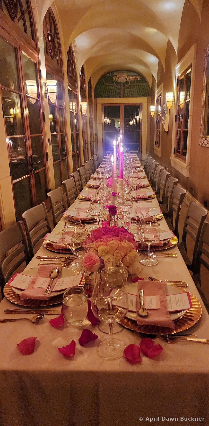A long table set for a large gathering, with candles, flowers and rose petals, in a room with arched ceilings