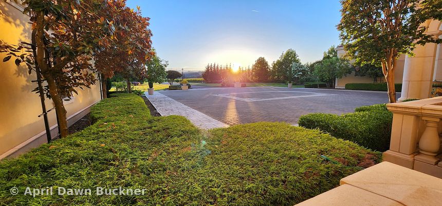 Sunset over the stone-paved courtyard, with hedges and a stone wall in the foreground