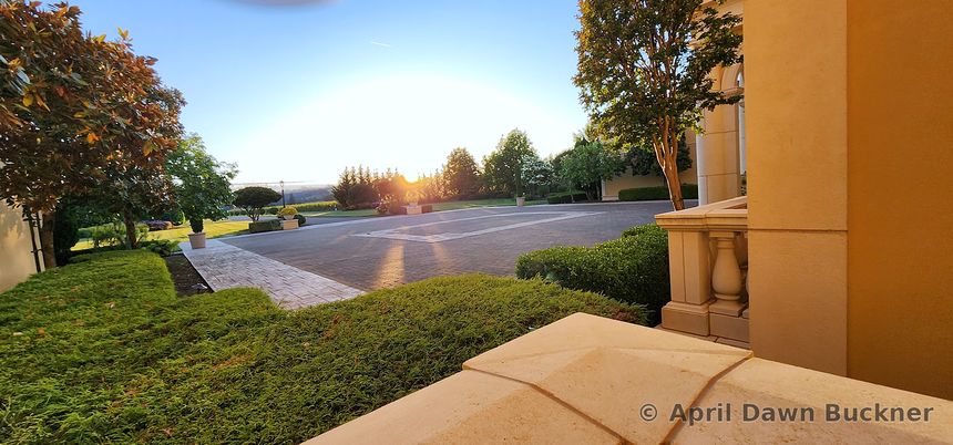 Looking out from a stone terrace over the courtyard and drive toward distant hills at sunset