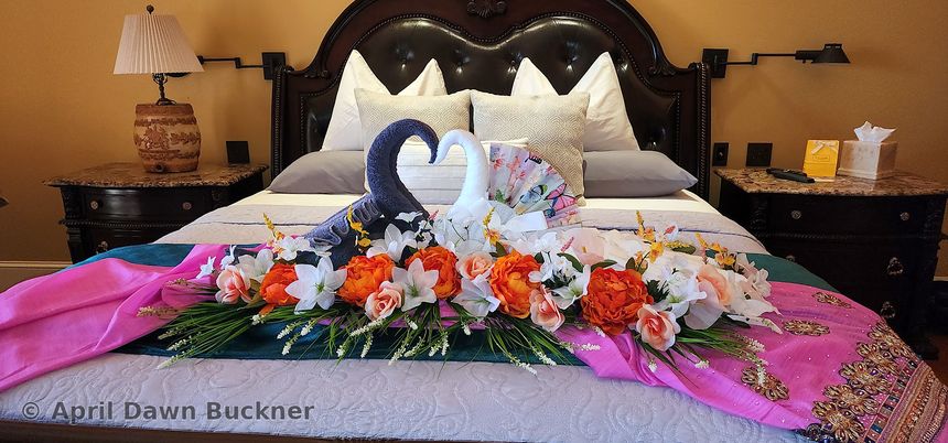 A bed with towel swans and pink, white and orange flowers