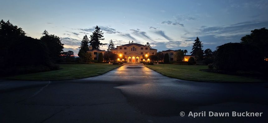 The villa lit up in the evening at the end of the paved drive