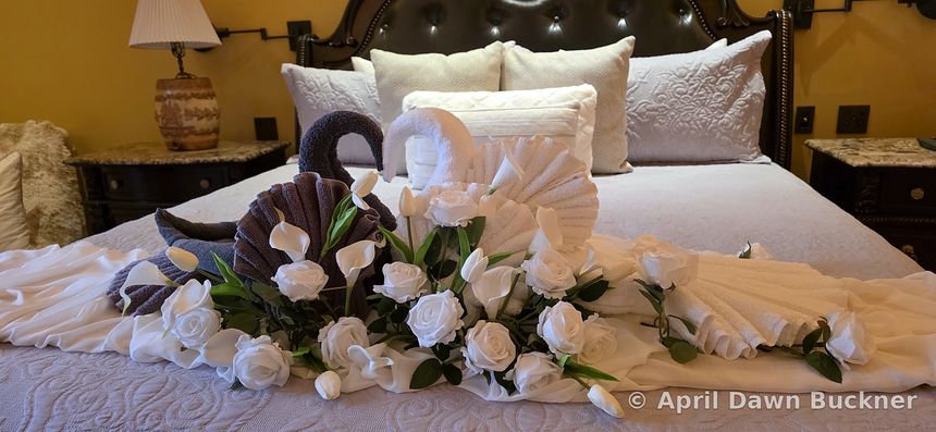 White towel swans among white roses on a bed