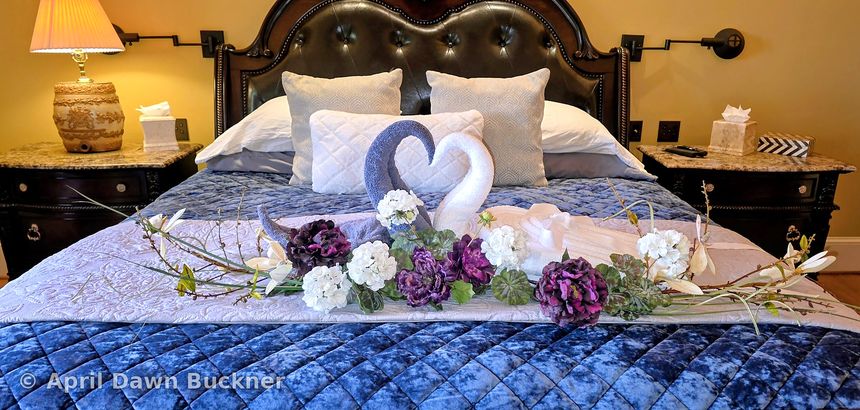 A bed with a blue velvet bedspread, towel swans and white and purple flowers